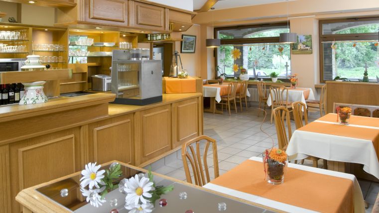 Un restaurant chaleureux avec une décoration en bois et des couleurs claires. Les tables sont simplement dressées et offrent une atmosphère accueillante.