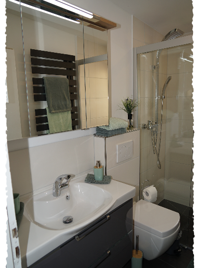 Une salle de bains moderne avec un lavabo, une douche et des carreaux lumineux. Les meubles sont dans des couleurs neutres et il y a des éléments décoratifs comme des serviettes et des plantes.