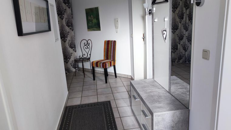 Ein heller Flur mit einem Spiegel und einer modernen Garderobe. Eine bunte Stuhl und ein Teppich sorgen für eine einladende Atmosphäre.