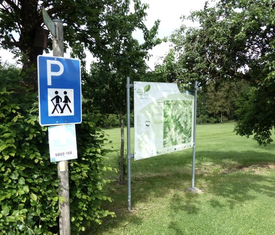 Parkplatzschild für Wanderer neben einer Informationstafel in grüner, bewaldeter Umgebung. Sonniger Tag, Bäume und Wiese im Hintergrund., © Tourist-Information Islek, Ingrid Wirtzfeld