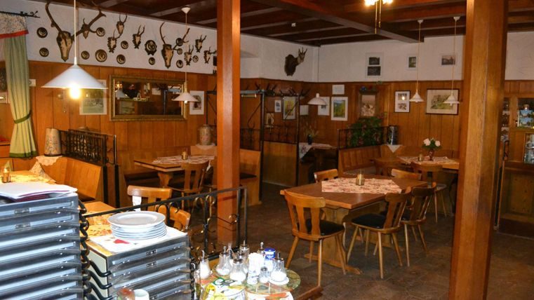 Un restaurant confortable avec des meubles en bois et des trophées de chasse aux murs. Il y a des tables mises et une salle accueillante pour les invités.