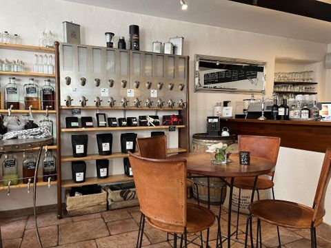 Ein gemütliches Café mit Holzmöbeln und einem Regal voller Tees und Gewürze. Die Wände sind hell und die Atmosphäre einladend.