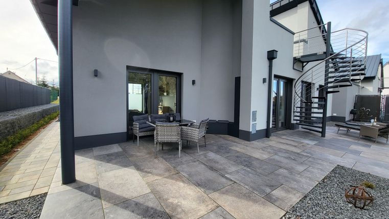 Une terrasse moderne avec des meubles confortables et une vue sur un bâtiment de deux étages. L'environnement est soigné avec des dalles en pierre et du gravier.