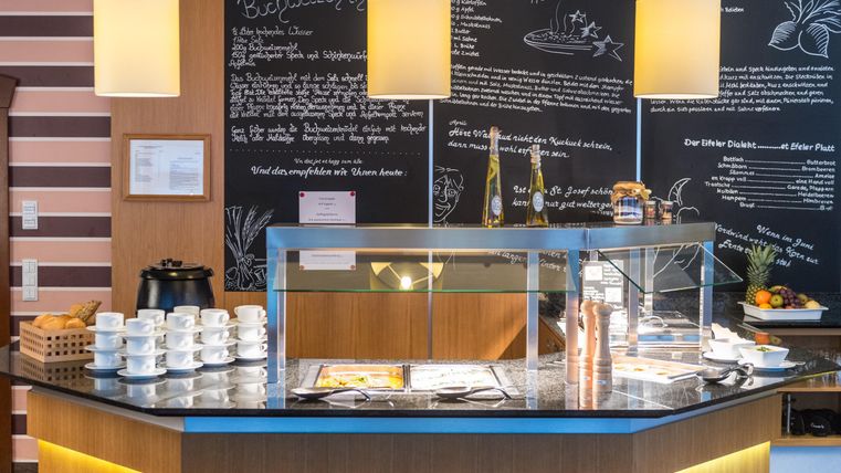 Een uitnodigende ontvangsthal met een elegante balie en veel koffiekopjes. Aan de muur zijn handgeschreven menu-aanbiedingen te zien.