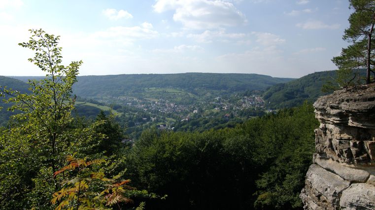 A picturesque view of a green landscape with hills and a small village in the valley. The sky is clear and the sun is shining.