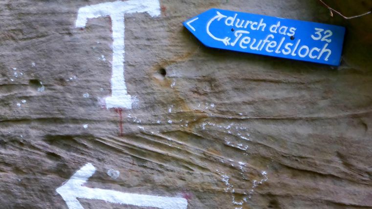 A rock with white arrows and a blue signpost. The signpost points towards "Devil's Hole".
