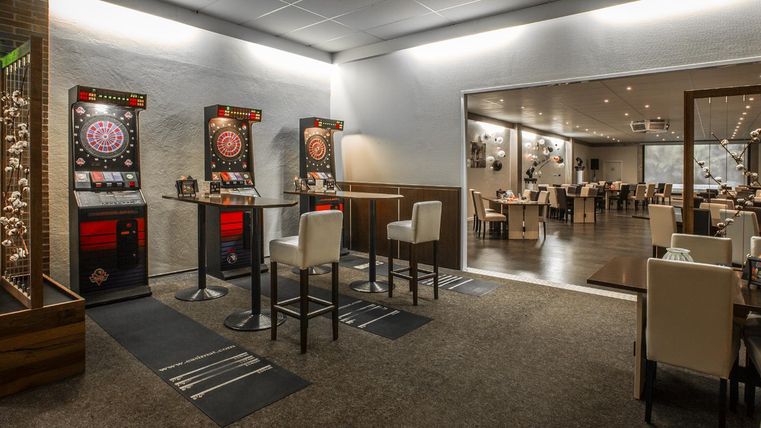 Ein modernes Restaurant mit einem Darts-Bereich und hellen Tischen. Der Raum ist freundlich eingerichtet und bietet Platz für Gäste.