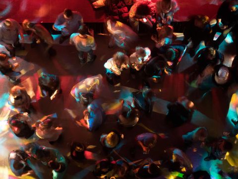 Eine lebhafte Tanzfläche mit vielen Menschen, die sich bewegen. Bunte Lichter werfen einen faszinierenden Schimmer auf die Szene.