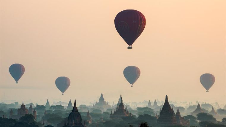 Heißeluchtballonnen stijgen boven een mistig landschap met tempels. De zachte kleurovergangen van de lucht creëren een rustige sfeer.