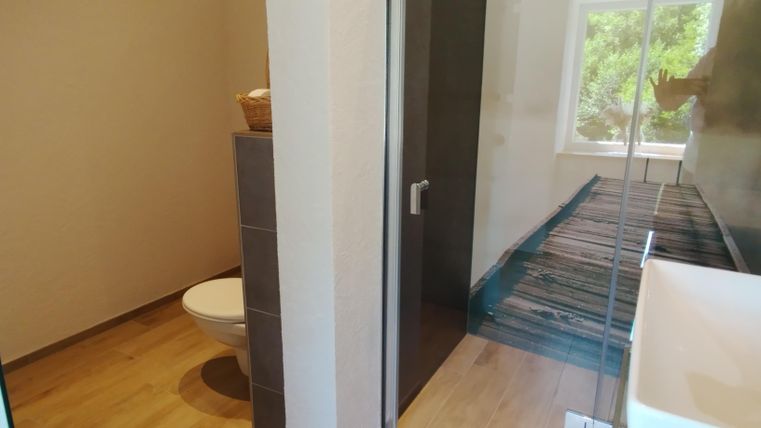 Een moderne badkamer met een toilet en een douche. De ruimte heeft een houten vloer en een raam met uitzicht op de buitenlucht.