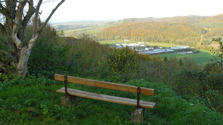 Banc en bois avec vue sur un paysage de collines et une zone industrielle.