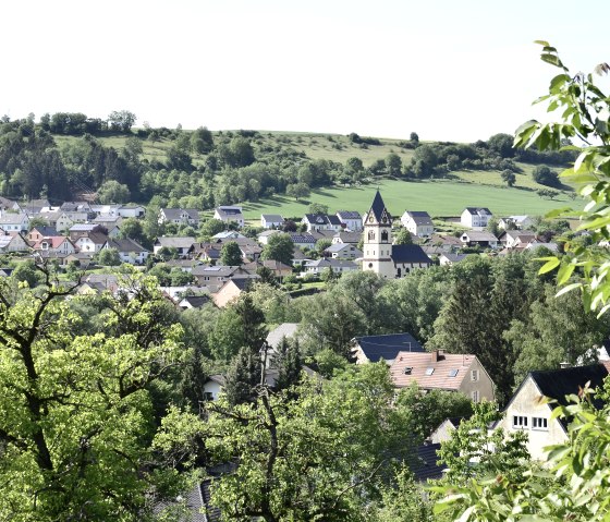 Panoramablick auf das Dorf Oberweis mit einer Kirche im Zentrum, umgeben von gr&uuml;ner Landschaft und B&auml;umen im Vordergrund., &copy; TI Bitburger Land