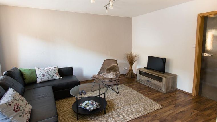 A modern living room with a comfortable sofa and a round glass table. A decorative plant and a television complete the room.