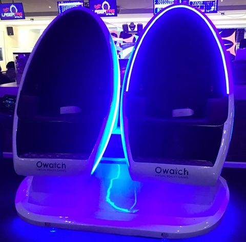 Deux sièges futuristes avec des lumières LED bleues douces. Ils se trouvent dans un complexe de divertissement et semblent destinés à la réalité virtuelle ou aux expériences immersives.