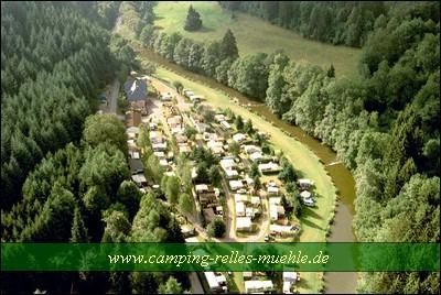 Un camping pittoresque le long d'une rivière, entouré de forêts verdoyantes. Le site propose des emplacements pour caravanes et tentes dans un cadre naturel.