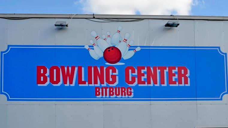 Ein großes Schild mit der Aufschrift "BOWLING CENTER BITBURG". Darauf sind Bowlingkugeln und Kegel abgebildet, vor einem blauen Hintergrund.