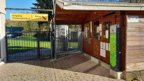 Ingang tot het recreatiezwembad met een houten gebouw en een hek. Op een bord staat "Ingang Recreatiezwembad" en "Kassa".