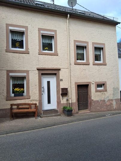 Une maison confortable sur une rue avec plusieurs fenêtres et une porte d'entrée. Devant la maison se trouve un banc et un pot de fleurs.