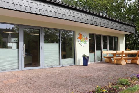 Un bâtiment moderne avec de grandes fenêtres et une entrée accueillante. Devant le bâtiment se trouve un banc en bois dans un jardin paisible.
