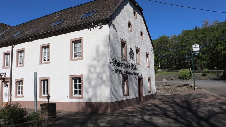 A historic building with a white facade and red windows. In the background, there are trees and a blue sky.
