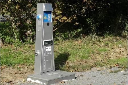 A parking meter in a green environment. It stands on a gravel path next to a lawn.
