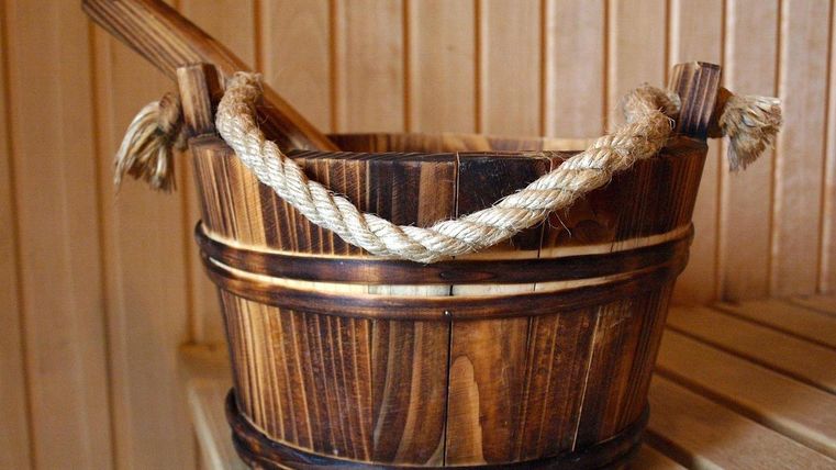 Ein Holzbehälter mit einem Seilgriff steht in einer Sauna. Die natürliche Holzfarbe passt gut zur Umgebung.