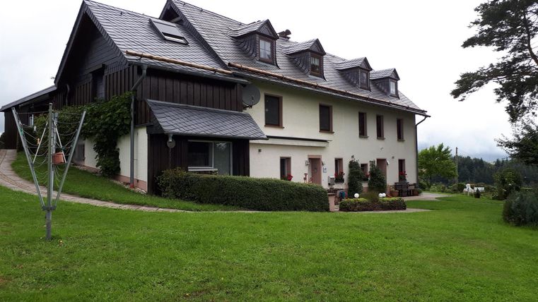 Une grande maison moderne avec un jardin verdoyant. Le ciel est nuageux et l'environnement est calme.