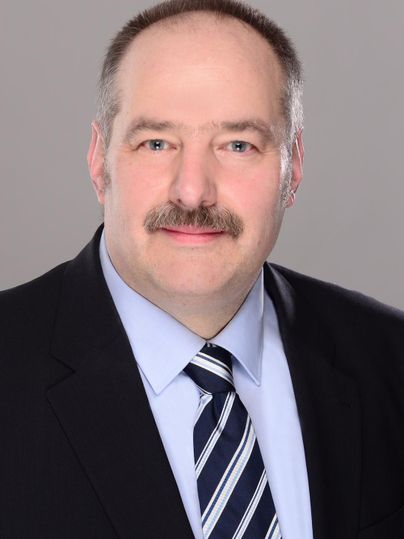 Zwei Männer sitzen in einem Raum. Sie lächeln und scheinen sich gut zu unterhalten.