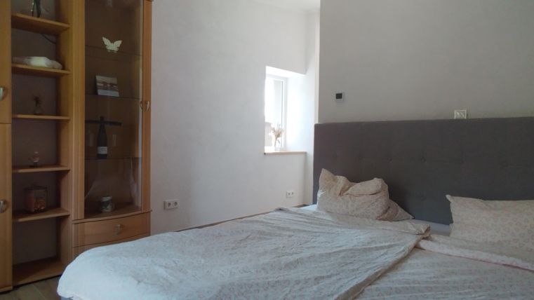 Een gezellige slaapkamer met een groot bed en een grijze hoofdbordwand. Aan de linkerkant staat een rolkasten met open planken.