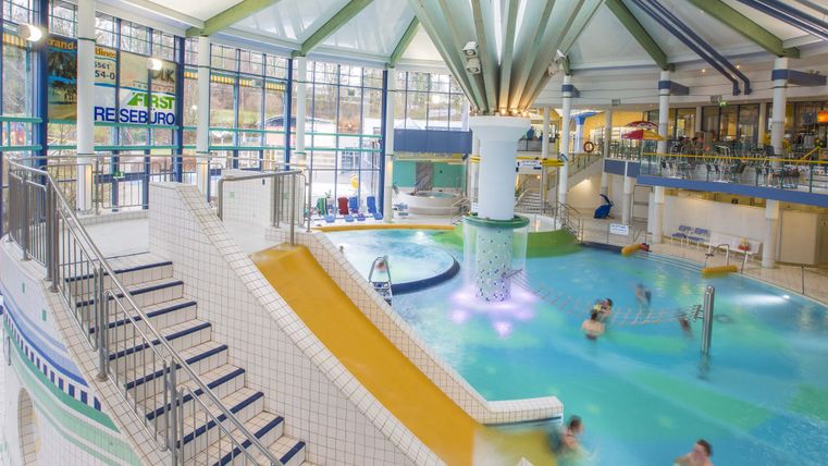 Een modern zwembad met een glijbaan en verschillende bassin. Veel mensen genieten van het water en de ontspannen sfeer.