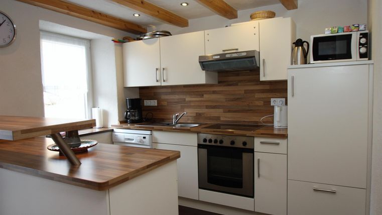 Eine moderne Küche mit weißen Schränken und einer Holzarbeitsfläche. Es gibt einen Herd, eine Spüle und verschiedene Küchengeräte.