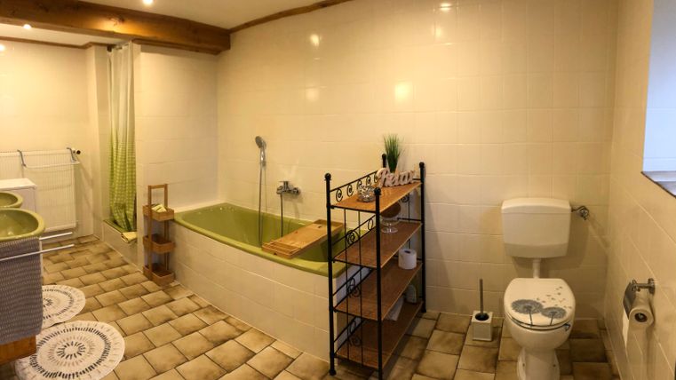 A bathroom with a bathtub, a toilet, and a shelf. The walls are brightly tiled, and the floor has an appealing tile texture.
