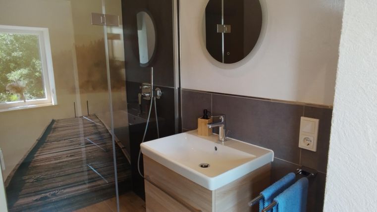 Een moderne badkamer met een glazen douche en een wastafel op een houten onderstel. Aan de muur hangt een ronde spiegel en een blauwe handdoekenhouder is zichtbaar.