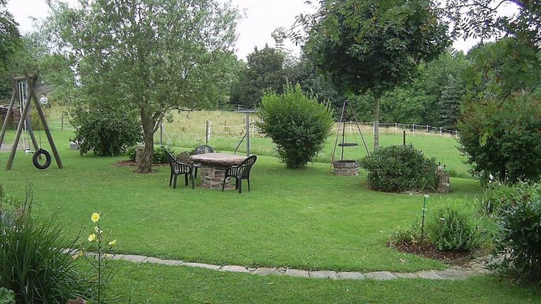 Ein schöner Garten mit Rasen, einem Tisch und Stühlen. Im Hintergrund sind Bäume und Schaukeln zu sehen.