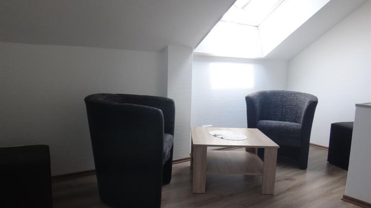 Une pièce confortable avec deux fauteuils et une table. Il y a une fenêtre de toit qui laisse entrer la lumière naturelle.