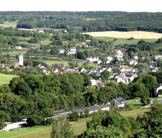 Panoramablick auf das Dorf Oberweis mit Kirche, umgeben von grünen Feldern und Wäldern im Bitburger Land., © P. J. Evertz