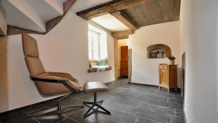 Ein gemütlicher Raum mit einem modernen Stuhl und großen Fenstern, die viel Licht hereinlassen. Die Wände sind hell und der Boden besteht aus dunklen Fliesen.