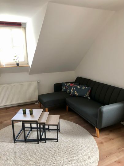 A cozy living room with a gray sofa and a small coffee table. The room has a bright atmosphere and a slanted ceiling.