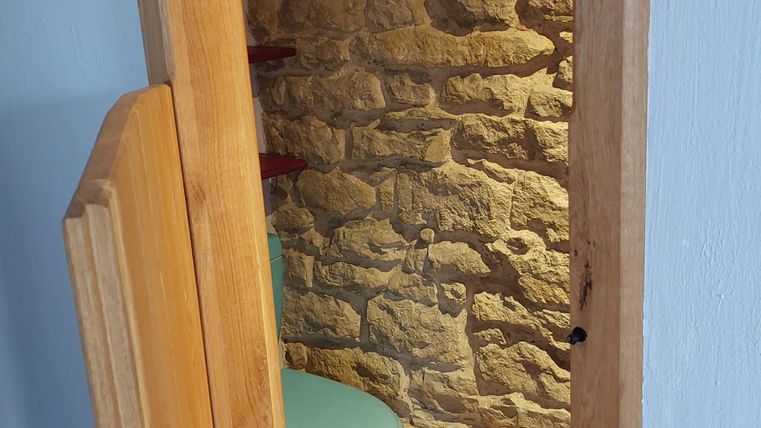 Een klein toilet met een moderne, turquoise toilet en een stenen muur. De ruimte heeft warm licht en een houten frame.