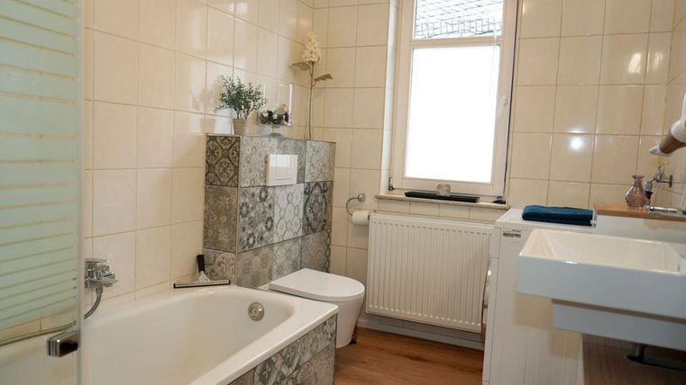 Een moderne badkamer met een bad en een wastafel. De elegante tegels en het houten design creëren een aantrekkelijke sfeer. Er is een wasdroger tot uw beschikking.