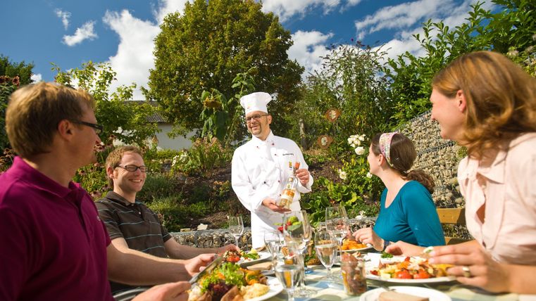 Un cuisinier sert un délicieux repas en plein air. Un groupe de personnes déguste le repas dans un bel environnement de jardin.