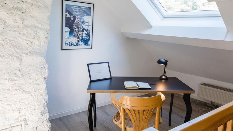 Ein gemütliches Arbeitszimmer mit einem Schreibtisch und einem Stuhl. Ein Fenster unter dem Dach sorgt für viel Tageslicht.