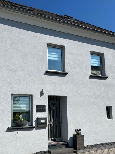 Une maison moderne, blanche, avec de grandes fenêtres et une porte d'entrée élégante. Le ciel est clair et bleu.