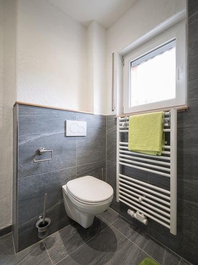 Une salle de bains moderne avec des toilettes et un porte-serviettes. La lumière du jour entre par la fenêtre, et une couleur de serviette verte apporte une touche fraîche.