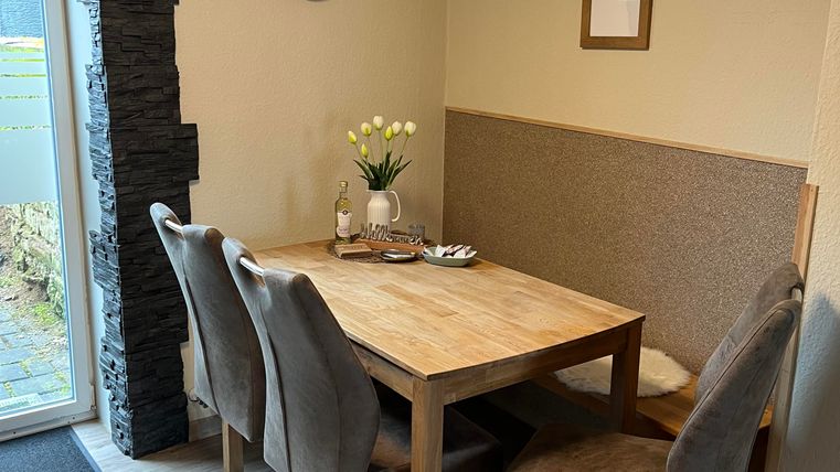 Un espace de repas confortable avec une table en bois et quatre chaises.
Sur le mur, il y a une horloge, et sur la table se trouve un vase avec des fleurs.