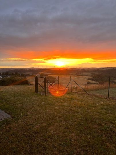Een prachtige zonsondergang boven een landschap met zachte heuvels. De lucht straalt in warme kleuren van oranje en geel.