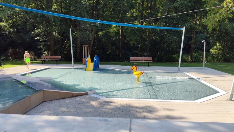 A water playground with a large flat water area. In the background, trees and benches can be seen.