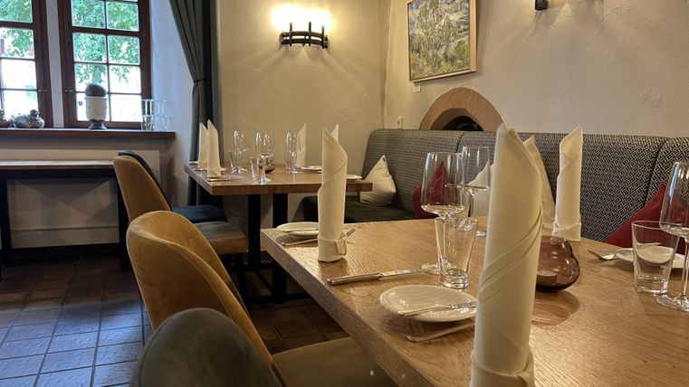 Un restaurant chaleureux avec des tables joliment dressées. Les murs sont clairs et il y a de grandes fenêtres qui laissent entrer la lumière du jour.