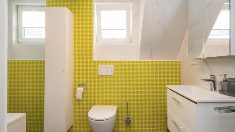 Une salle de bain moderne avec des carreaux jaunes et des meubles blancs. Il y a une fenêtre et une douche.