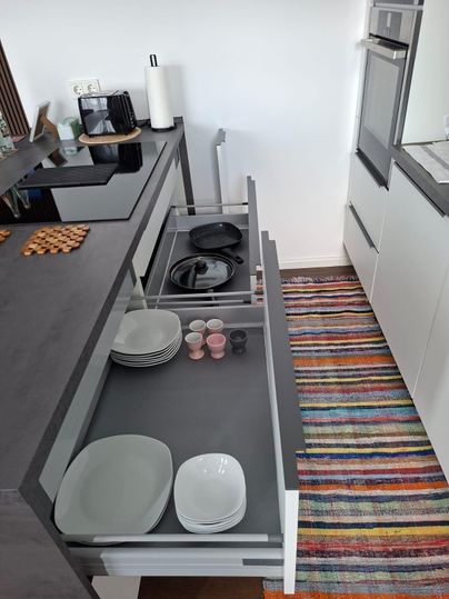 A modern kitchen with open drawers. Inside the drawers, plates, cups, and cooking utensils are neatly arranged.